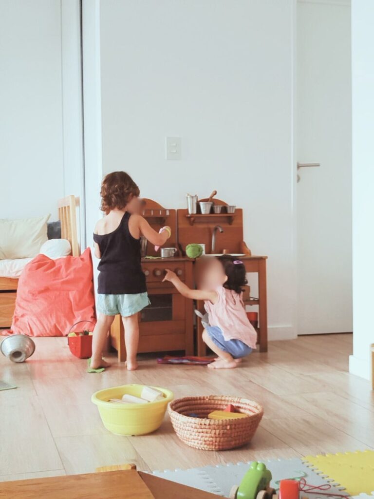 Niñas pequeñas utilizando la cocinita de madera Moulin Roty en espacio de juego libre