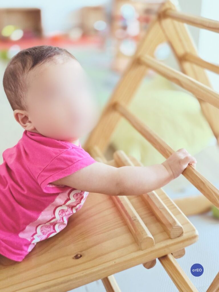 Bebé trepando por la rampa de un triángulo Pikler en un espacio de juego y movimiento libre.