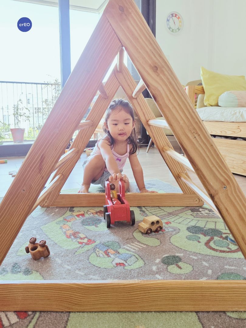 Niña pequeña descubriendo otros usos para el triángulo Pikler en un grupo de juego libre.