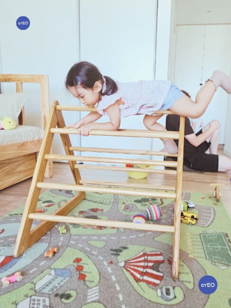 Bebés explorando un triángulo Pikler en un ambiente de movimiento libre, con espacio amplio alrededor.