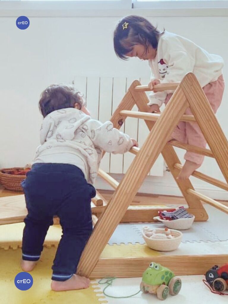 Niños de distintas edades usando un triángulo Pikler de diferentes maneras en un grupo de juego libre.