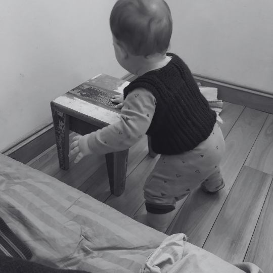 Bebé de pie sosteniéndose en un objeto bajo mientras experimenta el equilibrio y la fuerza.