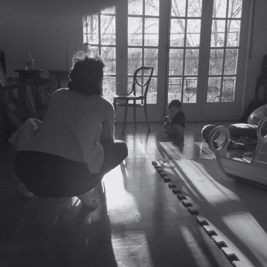 Adulto en el piso observando a un bebé que explora el espacio con libertad en un entorno hogareño.