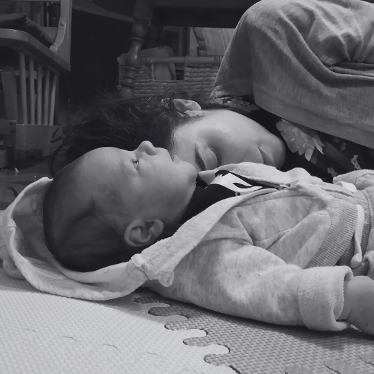 Adulto y bebé recostados en el piso compartiendo un momento de calma y presencia corporal.