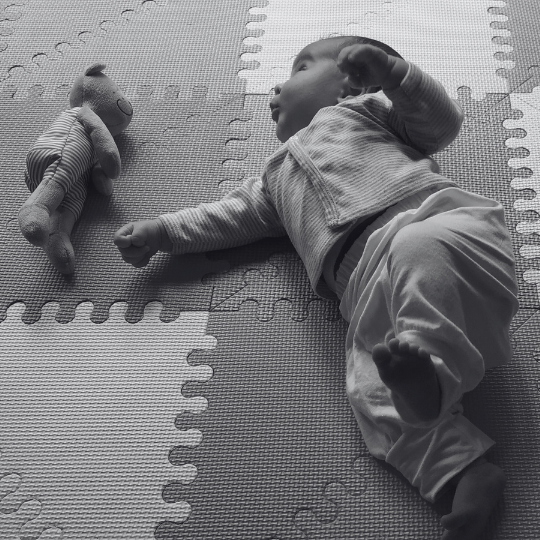 Bebé acostado boca arriba en el piso observando y moviendo su cuerpo en calma, ejemplo de movimiento libre bebés.