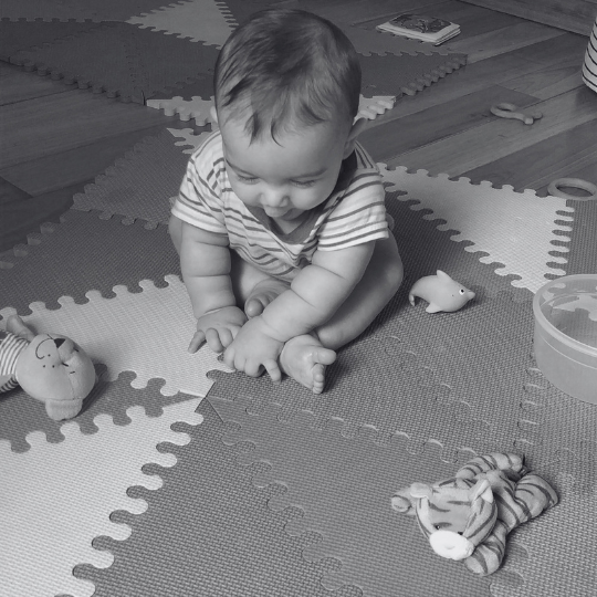 Bebé sentado en el piso explorando objetos y su propio cuerpo con atención sostenida.