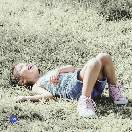 Niña recostada en el suelo riendo, disfrutando.