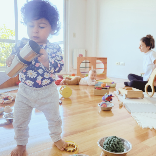 bebé que aún no gatea explorando en un grupo de juego libre acompañado junto a un adulto y otro bebé caminante