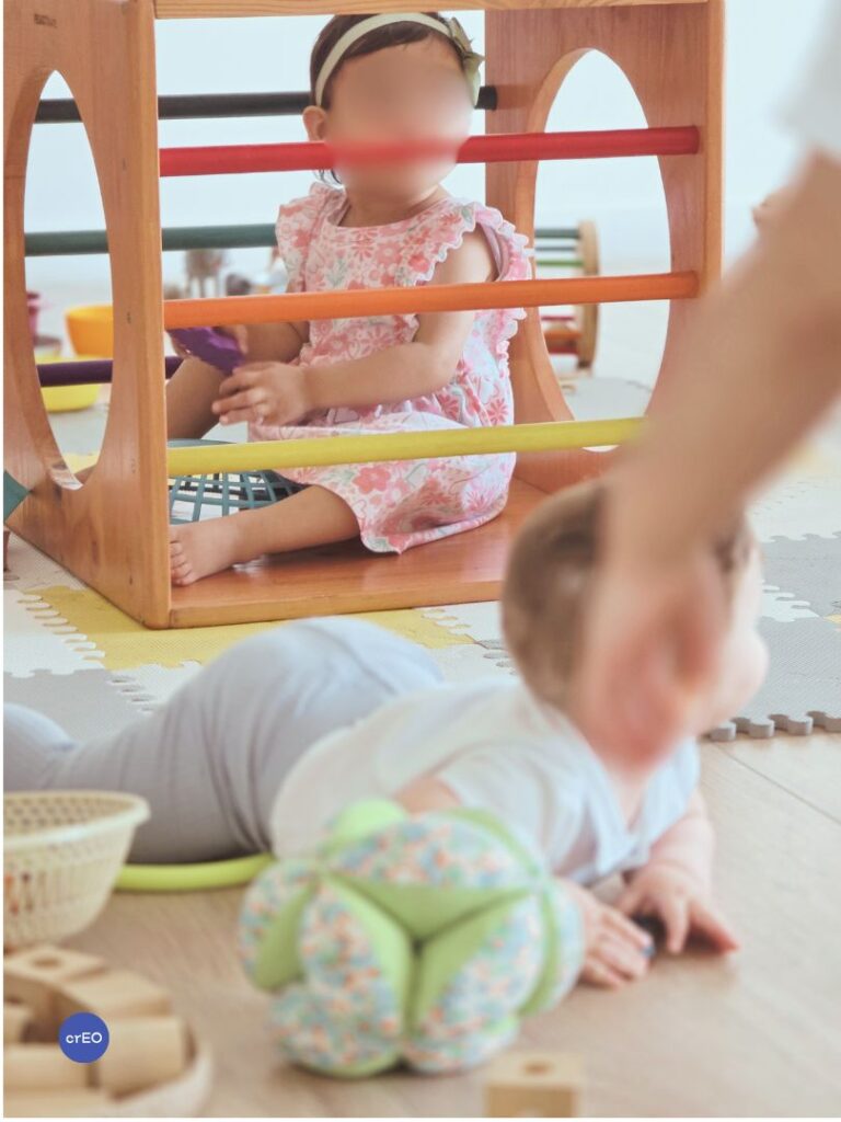 Bebé explorando un cubo Pikler de madera durante el juego libre, entrando y saliendo por sus aberturas.